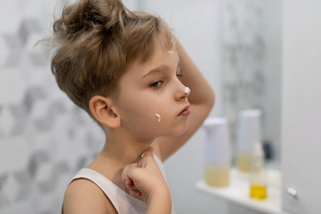 Child applying skincare in bathroom during morning routine with focus on self-care and hygiene practicesの写真素材