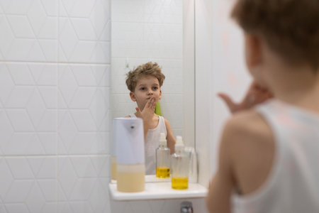Child explores skin care routine in bathroom mirror reflection during morning hoursの写真素材