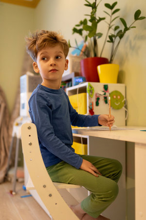 Young boy engaged in creative activity at colorful desk in a bright indoor space during daytimeの写真素材