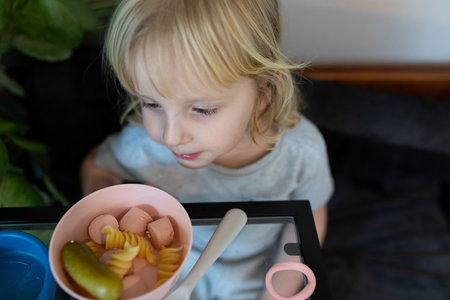 Child enjoying a colorful bowl of snacks featuring pickles, fruit, and candies during a casual indoor momentの写真素材