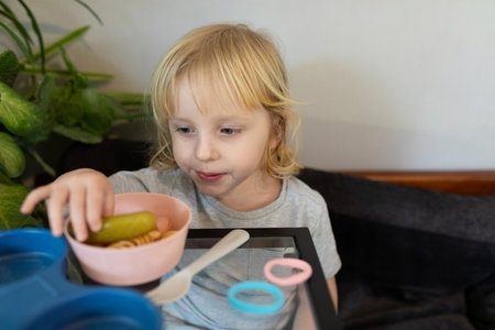 Young child enjoying a snack of pickles and crackers at home in a cozy setting during the afternoonの写真素材