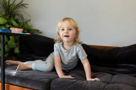 Joyful child playing on couch in cozy living room with plants in the background during sunny afternoonの写真素材