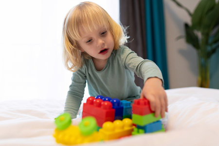 Child builds colorful structures with blocks on a bed in a cozy indoor setting during the afternoonの写真素材