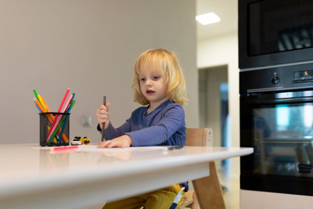 Child engaged in creative drawing at home with colorful supplies on a bright kitchen tableの写真素材