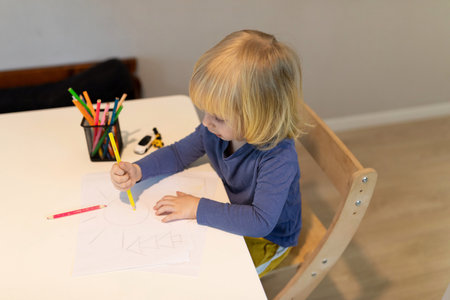 Child engaged in creative drawing activity at a bright indoor workspace during daytimeの写真素材