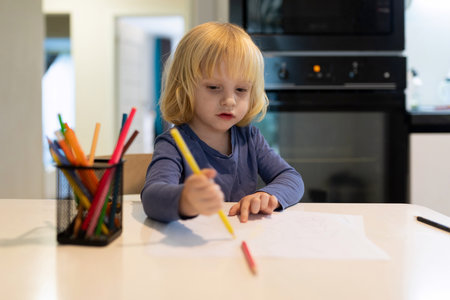 Child engages in creative drawing at kitchen table using colorful markers during daylight hoursの写真素材