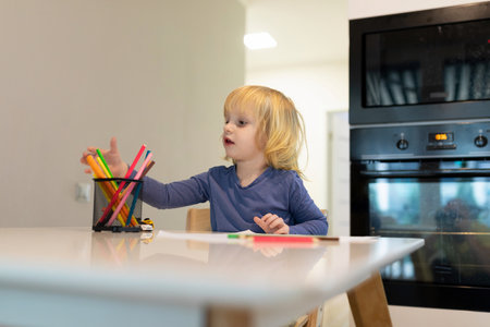 Child engages in creative drawing activity at a kitchen table with colorful markers in the morning lightの写真素材