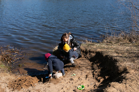 Children play by the riverbank while an adult supervises on a sunny day in early springの写真素材