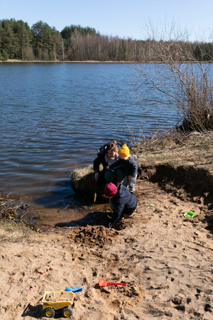 Children enjoy a sunny day playing by the lake, digging in the sand and using toys near the waters edge during springtimeの写真素材
