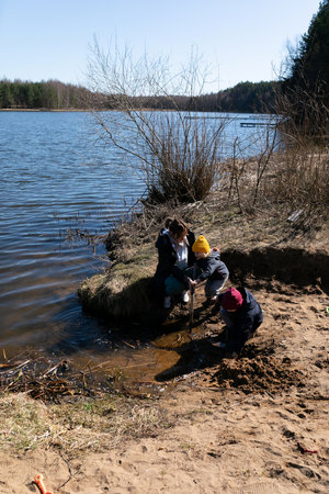 Children exploring a riverbank on a sunny spring day while engaging in playful activities near the waters edgeの写真素材