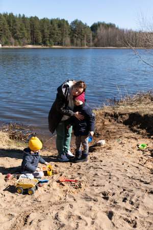 Children play on the sandy shore while a parent hugs one of them by the lakeside on a sunny day in springの写真素材