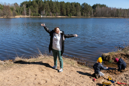Enjoying a sunny afternoon by the lake while children play in the sand near the waterの写真素材