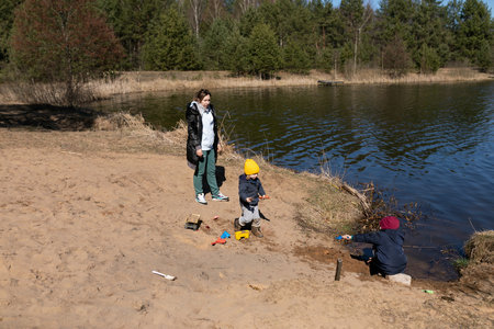 Mother and children enjoy a sunny day at the lake, playing in the sand and water on a warm afternoon in springの写真素材
