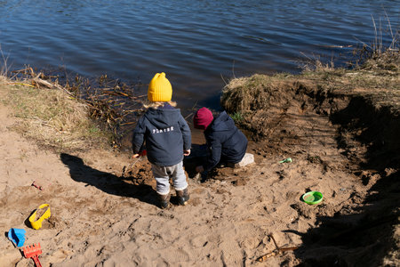 Children enjoy playtime by the riverbank, building sand structures during a sunny afternoon in early springの写真素材