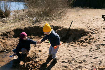 Children play by a sandy riverbank in early spring, engaging in creative outdoor activities and enjoying natureの写真素材