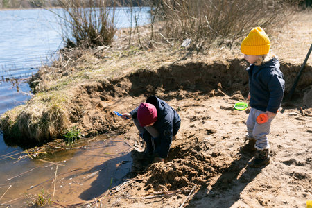 Children dig in the sand by the riverside on a sunny day in early springの写真素材