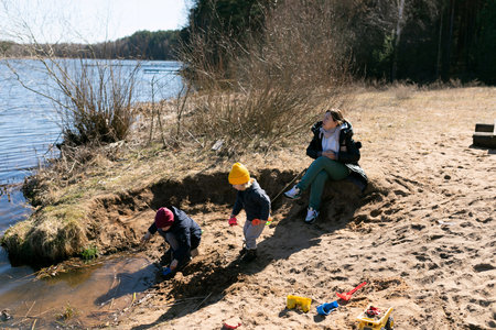 Children playing in sand by the lake while adult supervises on a sunny day in springtimeの写真素材