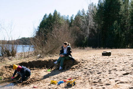 Family enjoys a day at the riverbank with children playing in the sand on a sunny spring dayの写真素材