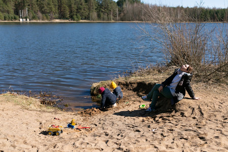 Children enjoying a sunny day at the lakeside while one adult relaxes nearbyの写真素材