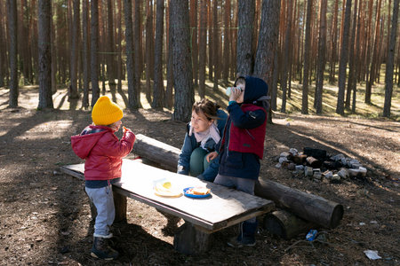 Family enjoys a picnic in the forest with children playing and eating snacks on a sunny dayの写真素材