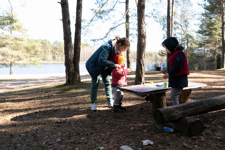 Family enjoys outdoor playtime while preparing snacks by a lakeside in a peaceful forest settingの写真素材