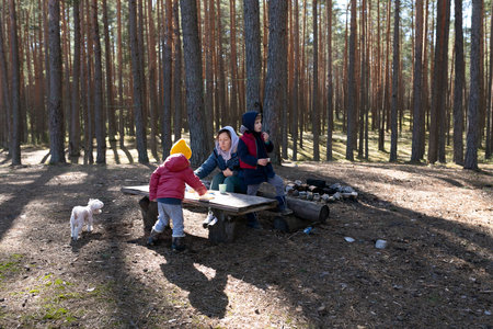 Children enjoy outdoor fun while playing and eating at a picnic table in a forest during a sunny afternoonの写真素材