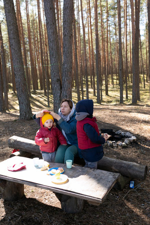Family enjoys a peaceful moment in the forest during a sunny autumn day while having snacks at a wooden tableの写真素材