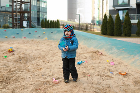 Child playing in a sandy area with toys on a sunny day in an urban environmentの写真素材