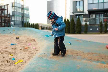 Young child playing in a sandpit at a modern playground during a sunny day in autumnの写真素材
