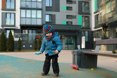 Child playing with toys on playground of modern residential building during winter afternoonの写真素材