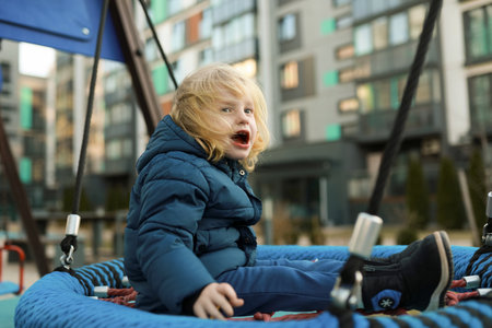 Child joyfully playing on a swing at a modern urban playground in the early afternoonの写真素材