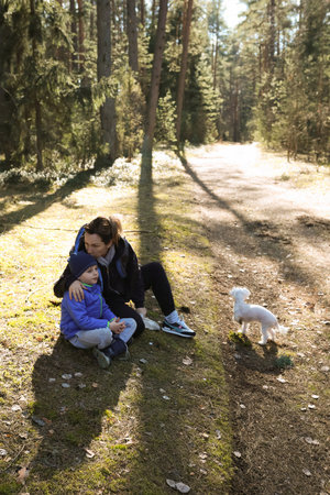 Mother and child enjoying a sunny day outdoors on a forest path with a small dog nearbyの写真素材