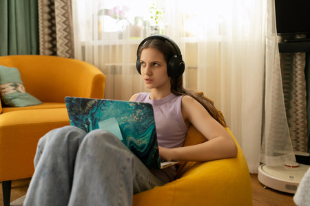 Young woman working on laptop, focused and relaxed in cozy living room with yellow chair during daytime hoursの写真素材