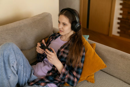 Female gamer enjoying video games on a sofa in a cozy living room during the eveningの写真素材