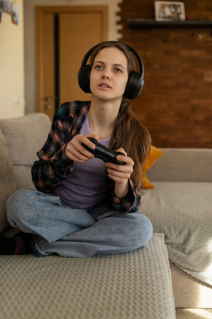 Girl wearing headphones plays video games indoors in a cozy living room surrounded by warm lighting