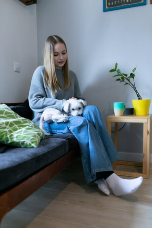 Woman sitting on a couch with a small dog on her lap in a cozy living room during daytime