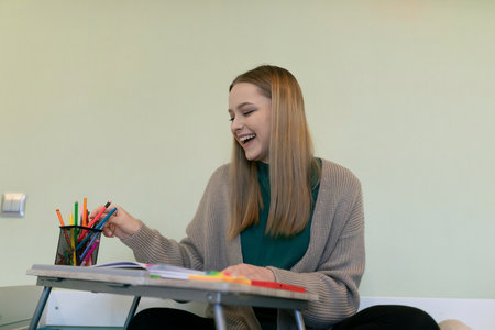 Young woman enjoying creative time while organizing colorful pens at a study desk in a bright indoor spaceの写真素材