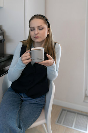 Young woman enjoying beverage in a modern kitchen while seated on a stylish chair in a cozy atmosphere during the afternoonの写真素材