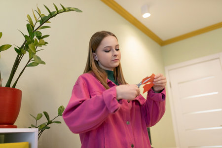 Young woman engages in creative paper cutting activity indoors in a colorful room during the daytime