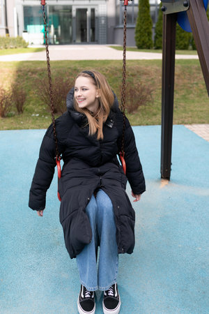 Young woman enjoying a swing in a park on a sunny day while dressed in casual winter attireの写真素材