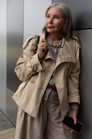 Stylish older woman poses elegantly near modern building in daytimeの写真素材