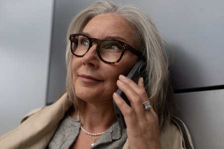 Senior woman smiles while talking on her smartphone in a modern urban setting during the afternoon