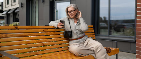 Woman sitting on wooden bench outside modern building while using smartphone during cloudy day
