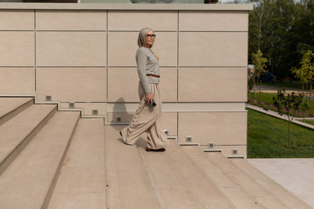 Elderly woman walks confidently down steps in a modern outdoor space during a sunny afternoon strollの写真素材