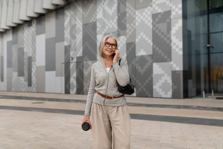 Smiling senior woman enjoying a phone call outside a modern building in the afternoonの写真素材