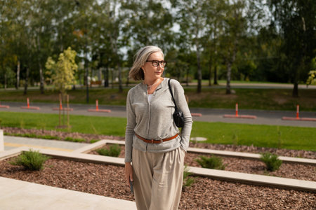 Elegant woman enjoying a sunny day outdoors while wearing stylish attire and posing near landscaped...