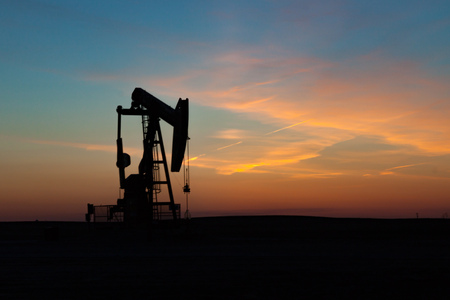 A single oil well pumpjack silhouetted against a prairie sunsetの写真素材
