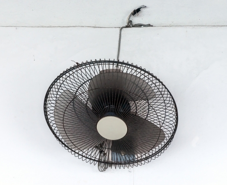 Black electric fan is hanging on the white wall.の写真素材
