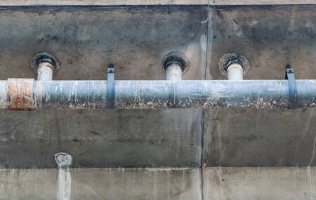 Rusty metal drain is hanging under the road bridge.