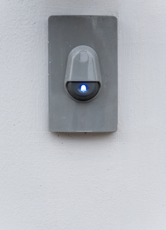Modern eletric buzzer with blue symbol on the white wall.